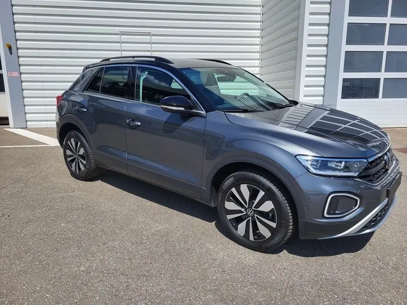 Volkswagen T-Roc gris Indium en 3/4 avant droit, avec jantes alliage et toit noir brillant visible.