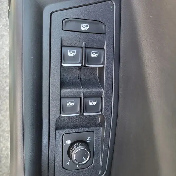 Vue rapprochée des commandes de lève-vitres et réglage des rétroviseurs côté conducteur du Volkswagen T-Roc gris Indium 2025.