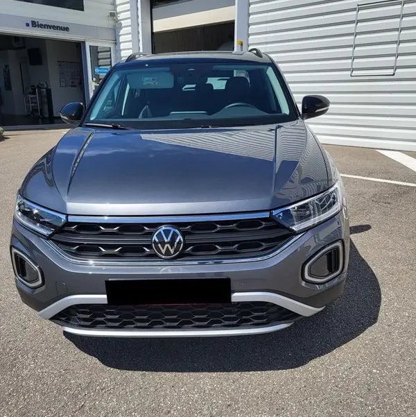 Vue avant d'un Volkswagen T-Roc gris Indium 2025, mettant en valeur la calandre chromée et les phares LED distinctifs.
