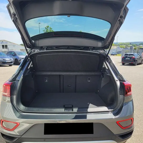 Vue arrière du Volkswagen T-Roc gris Indium 2025 avec coffre ouvert, montrant l'espace de chargement vide et l'attelage amovible.
