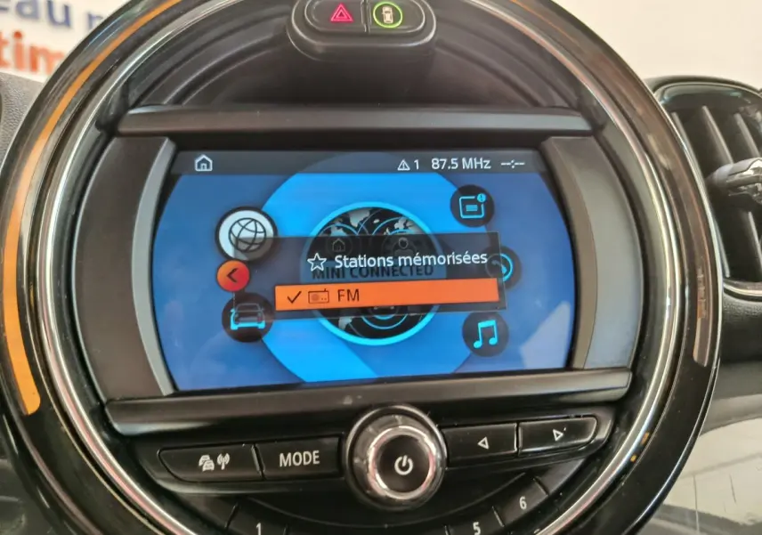 Gros plan sur l'écran central rond du MINI Countryman noir 2019 affichant le menu radio FM et commandes autour.