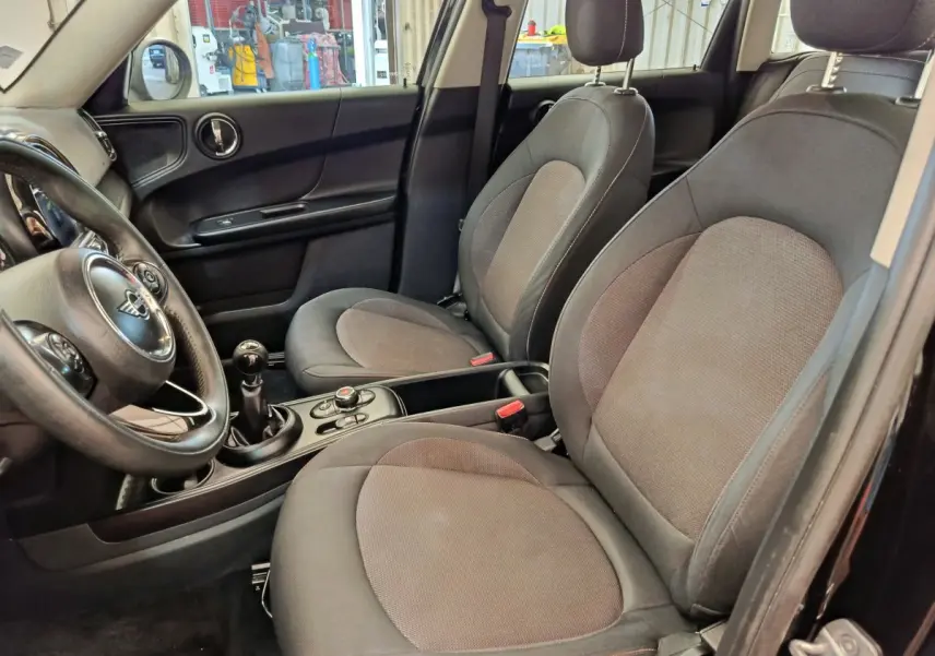 Vue intérieure côté conducteur de la MINI Countryman noire 2019, sièges tissu gris et volant cuir multifonctions.