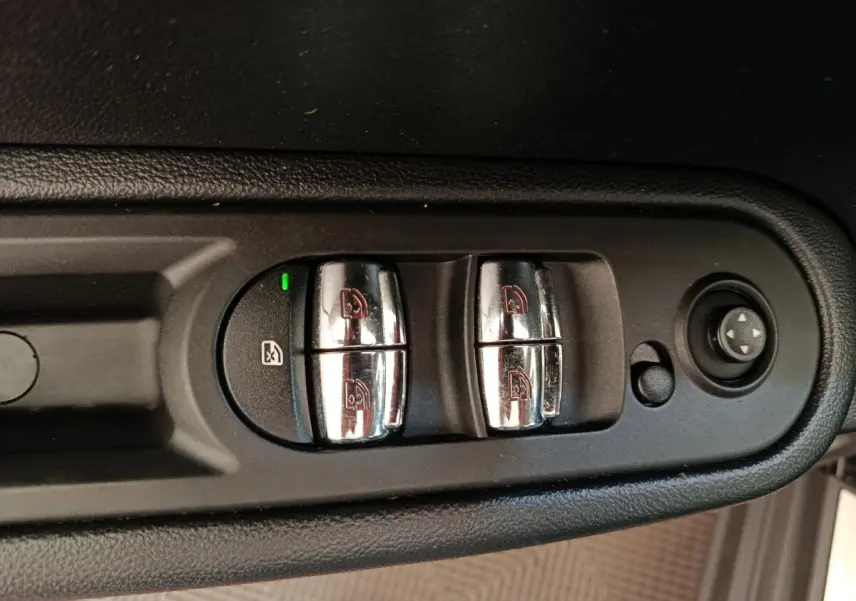Gros plan sur les commandes chromées des lève-vitres et réglages des rétroviseurs côté conducteur d'une MINI Countryman noire.