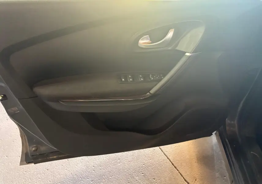 Vue intérieure côté gauche de la porte avant d’un Renault Kadjar gris avec commandes de vitres et poignée argentée.