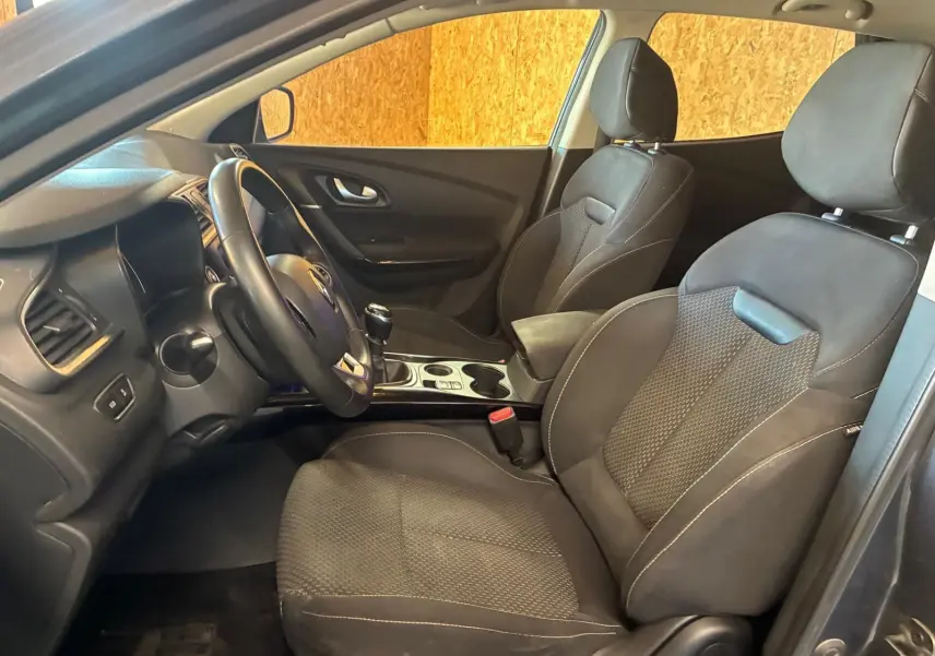 Vue intérieure côté conducteur du Renault Kadjar gris 2019, sièges tissu noir et volant avec boîte manuelle.