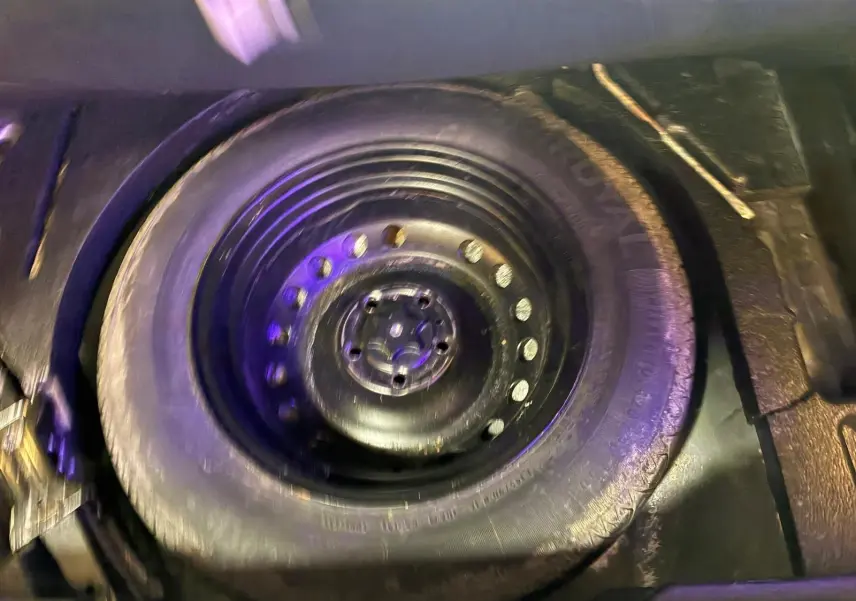 Roue de secours noire dans le coffre d'un Renault Kadjar gris, vue en plongée sur le pneu et la jante acier.