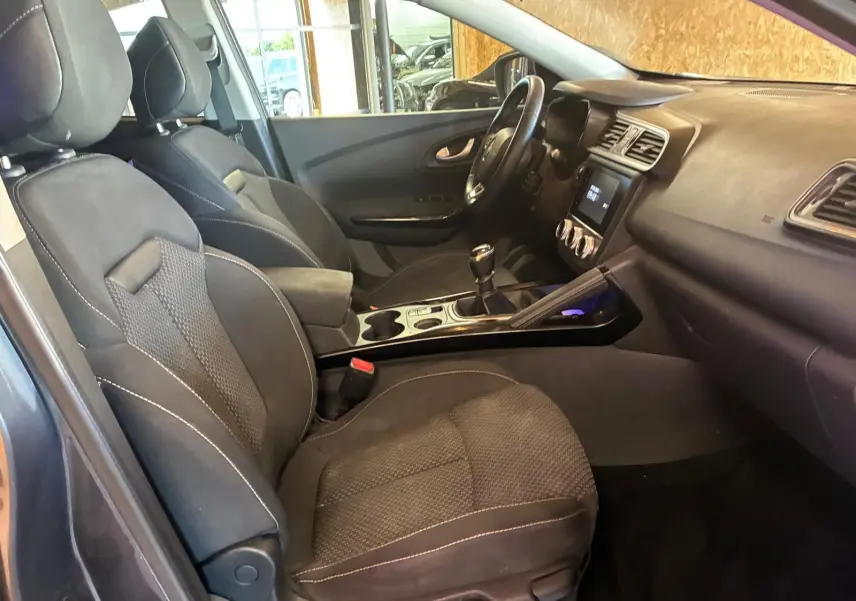 Vue intérieure côté conducteur du Renault Kadjar 2019, sièges tissu noir et tableau de bord avec écran tactile.