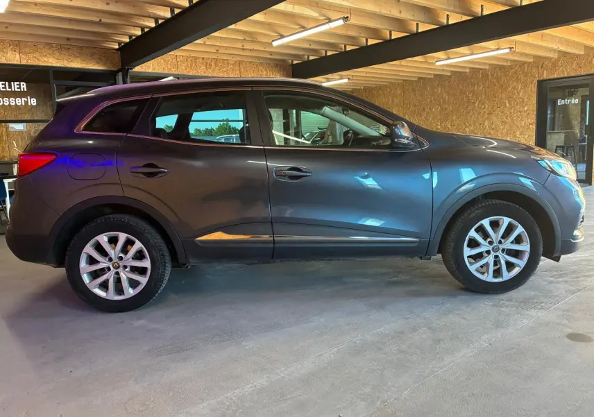 Vue de profil côté gauche d'un Renault Kadjar gris 2019 stationné en intérieur avec jantes alliage visibles.