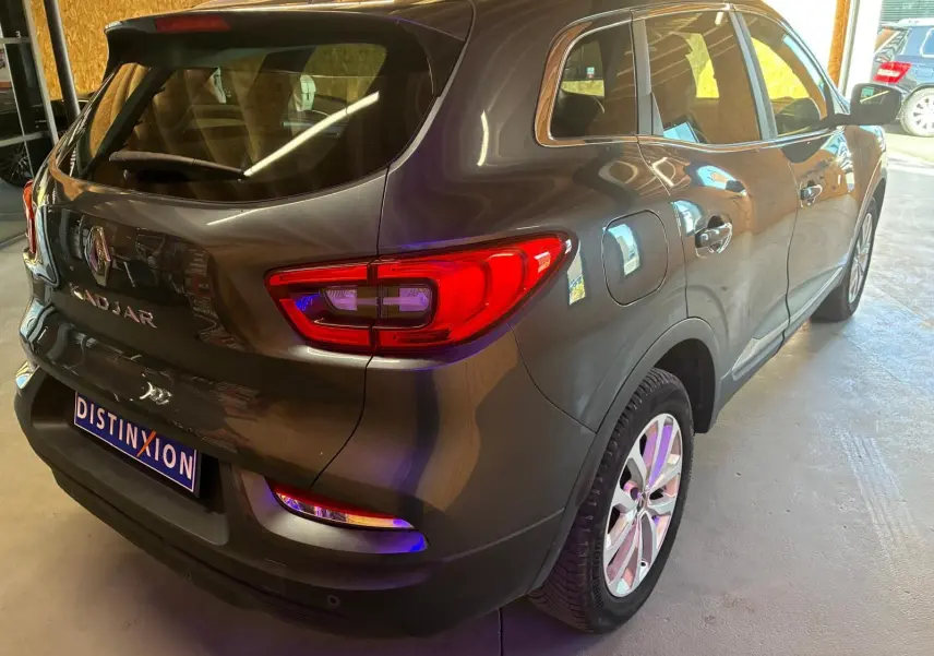 Vue 3/4 arrière droit d'un Renault Kadjar gris métallisé garé en intérieur avec feux arrière allumés.