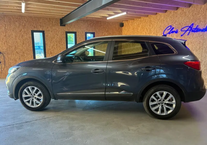 Profil côté gauche d'un Renault Kadjar gris 2019 stationné en intérieur, avec jantes alliage et vitres teintées.