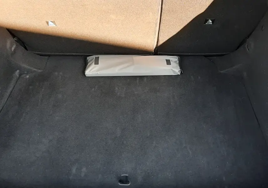Coffre ouvert vu de face d’une Peugeot 308 III Hybrid gris Artense, avec tapis noir et trousse blanche posée au fond.