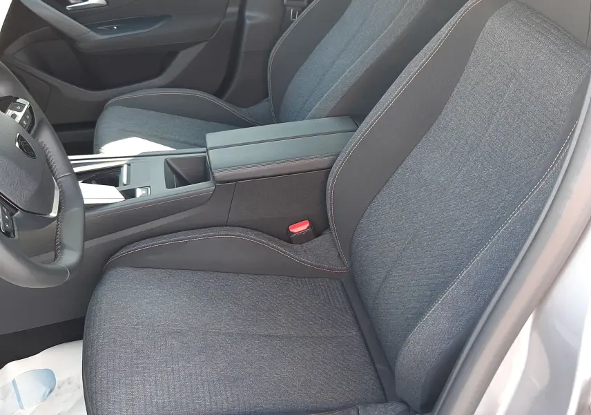 Intérieur avant droit de la Peugeot 308 gris Artense, sièges tissu gris avec surpiqûres orange et accoudoir central.