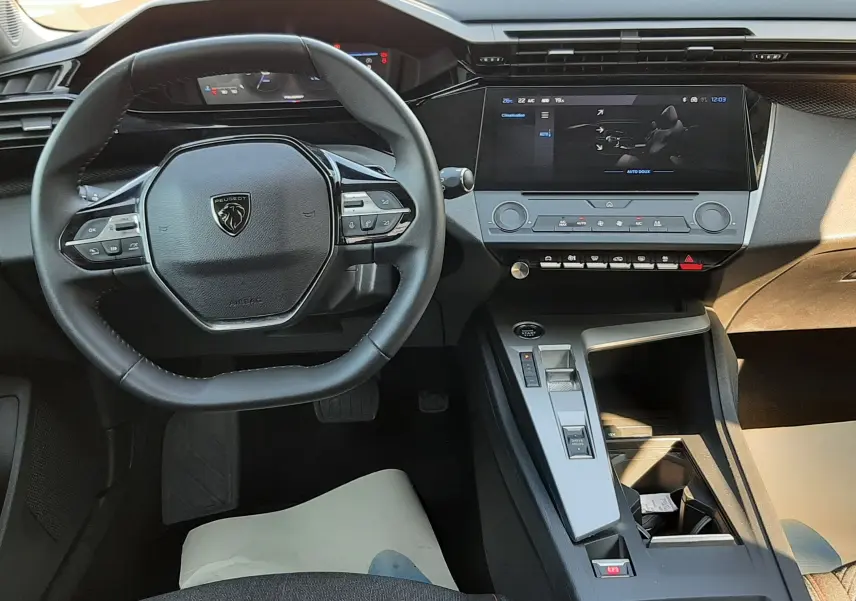Vue intérieure centrée sur le volant et la console centrale de la Peugeot 308 III Hybrid gris Artense, avec écran tactile et commandes intégrées.