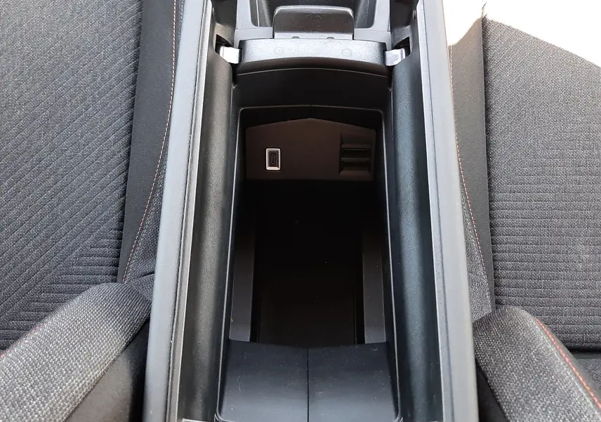 Vue plongeante sur le rangement central ouvert de la Peugeot 308 gris Artense, avec prises USB visibles entre les sièges avant en tissu noir.