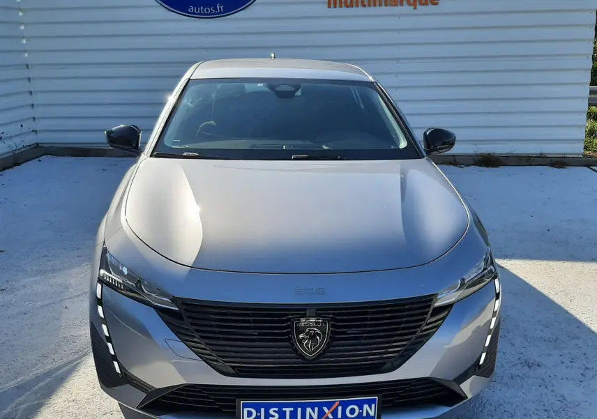Vue avant d'une Peugeot 308 III Hybrid gris Artense avec calandre noire et feux LED verticaux allumés.