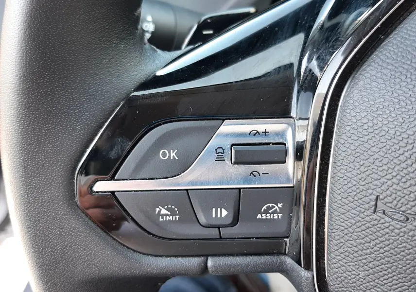 Gros plan sur les commandes gauche du volant noir du Peugeot 308 III Hybrid 145ch Style 2025, boutons de régulateur et assistance.