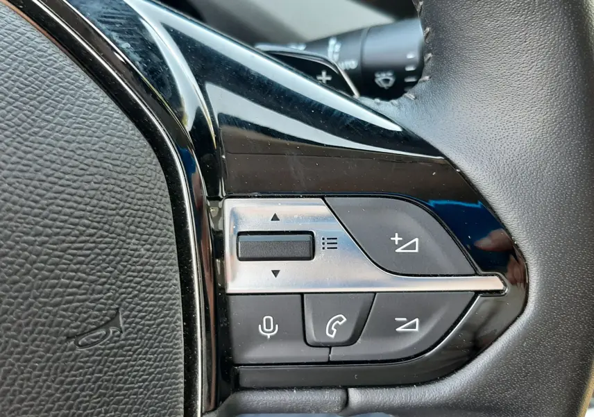 Gros plan sur les commandes multifonctions à droite du volant noir de la Peugeot 308 III Hybrid 145ch Style.