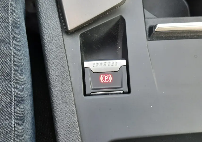 Gros plan sur le bouton de frein à main électrique rouge dans la console centrale noire d’une Peugeot 308 III Hybrid 2025.