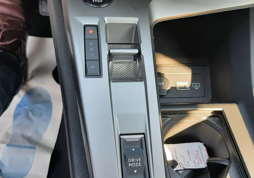 Vue rapprochée de la console centrale grise de la Peugeot 308 III Hybrid 145ch, avec sélecteur de mode de conduite et bouton start/stop.