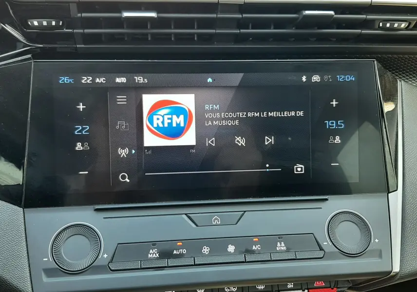Vue rapprochée de l’écran tactile et de la console centrale noire du Peugeot 308 gris Artense, affichant la radio RFM.