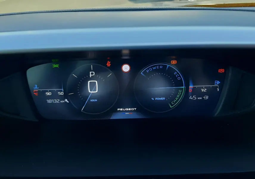 Tableau de bord numérique de Peugeot 308 III Hybrid gris, affichant vitesse à zéro et indicateurs de charge et autonomie.