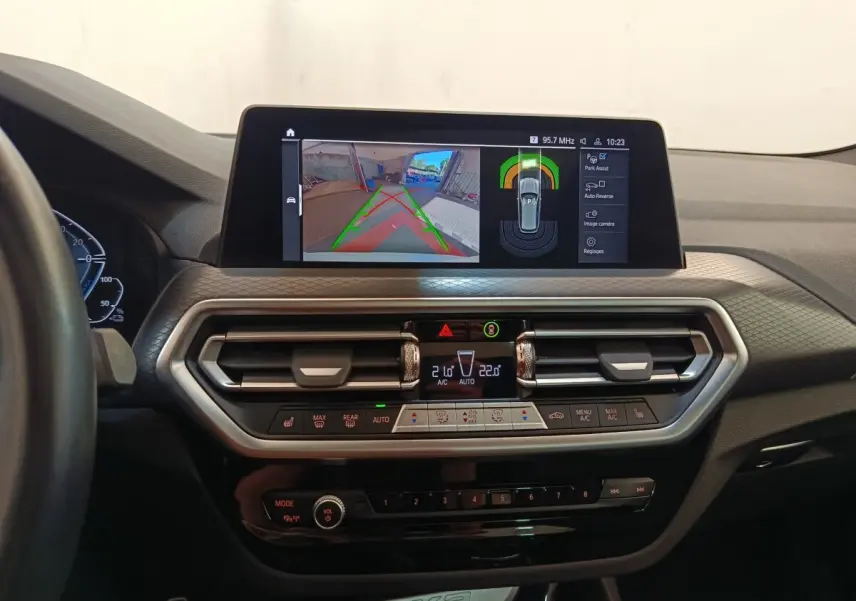 Vue intérieure du tableau de bord du BMW X3 blanc 2023 avec écran tactile affichant l'aide au stationnement.