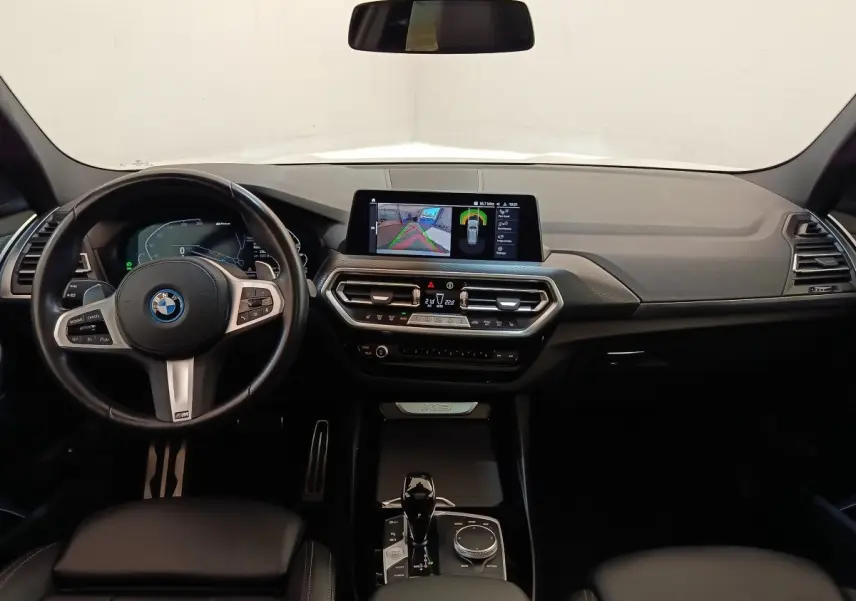 Vue intérieure avant du tableau de bord noir du BMW X3 xDrive30e avec écran tactile central et volant multifonction.