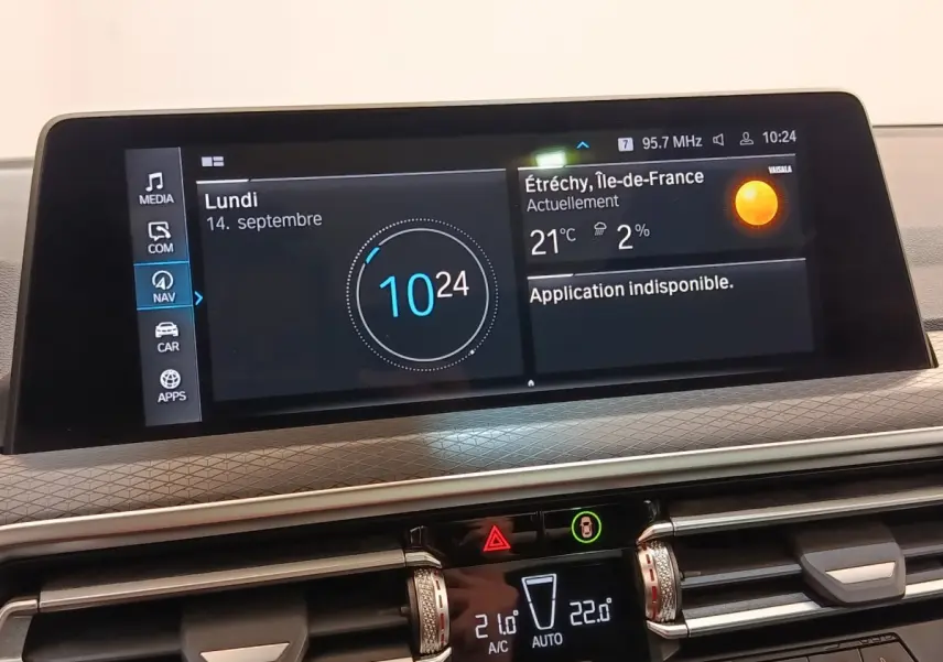 Vue rapprochée du tableau de bord numérique du BMW X3 blanc, affichant l’heure et la météo sur écran tactile.