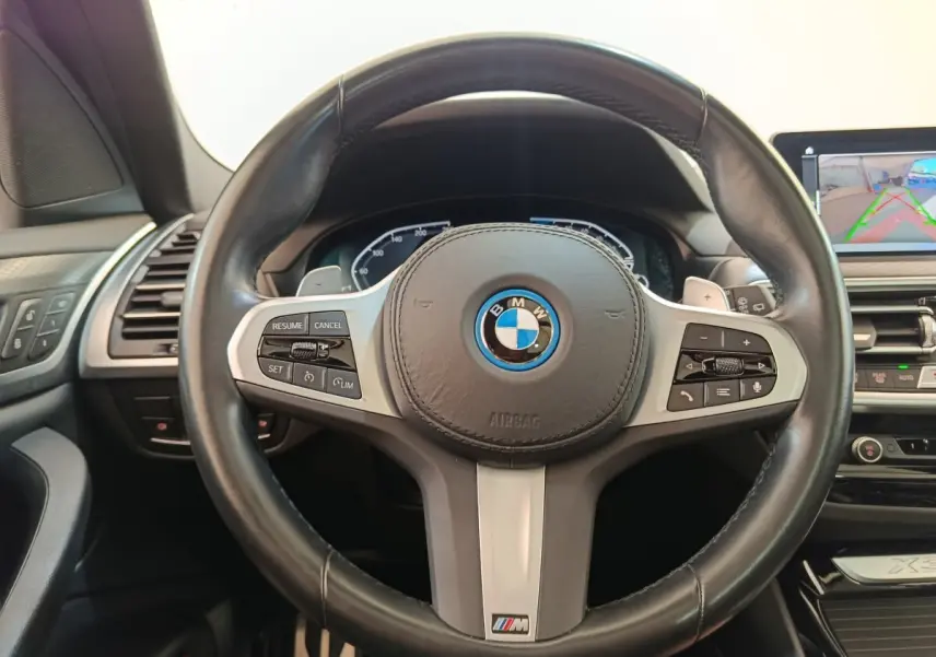 Vue rapprochée du volant cuir noir BMW X3 xDrive30e 2023 avec commandes multifonctions et logo M Sport.