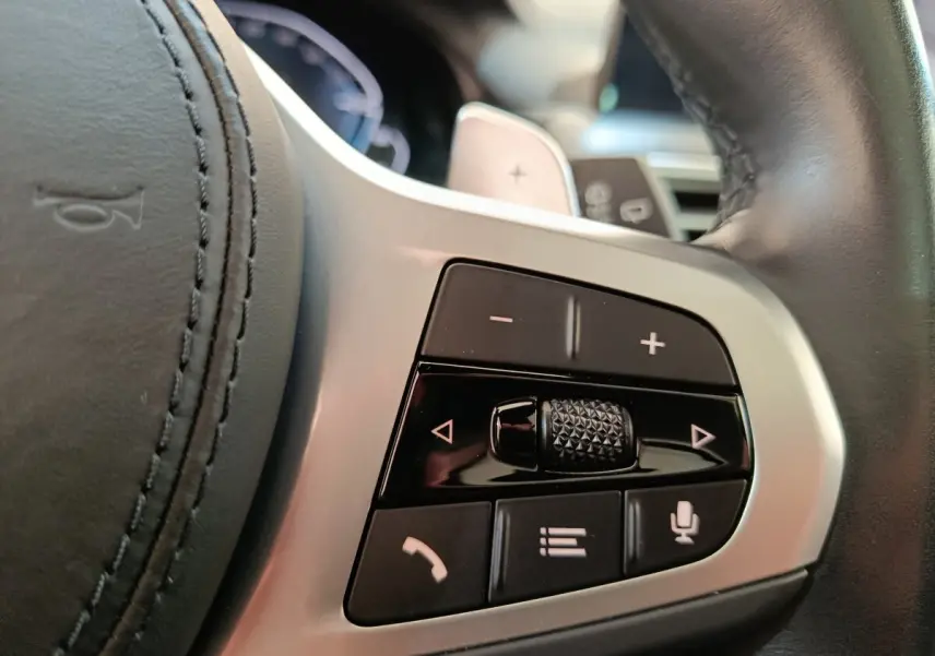 Gros plan sur les commandes du volant en cuir noir du BMW X3 blanc, avec boutons de volume et téléphone.