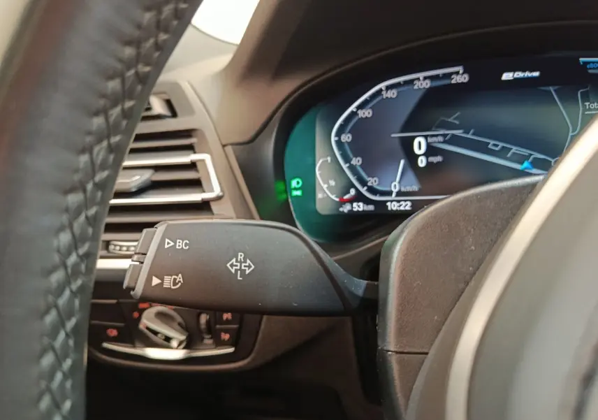 Gros plan sur le combiné d'instruments digital et la commande de clignotants du BMW X3 blanc xDrive30e 2023.