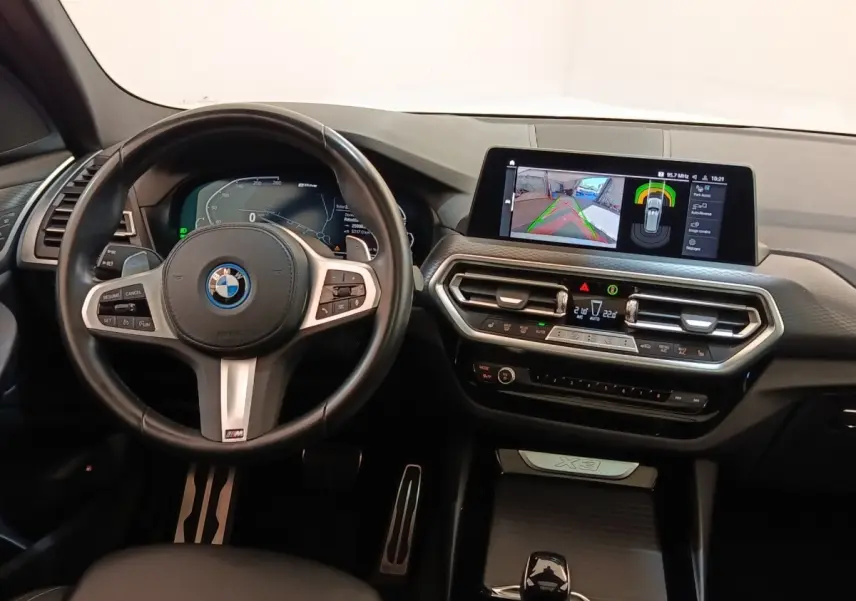 Vue intérieure du tableau de bord et volant cuir noir du BMW X3 xDrive30e avec écran tactile central allumé.