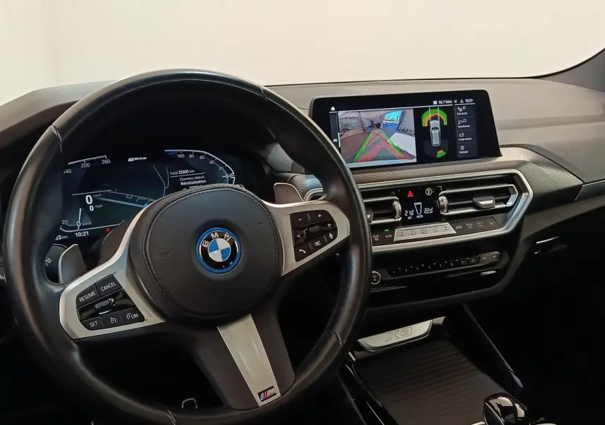 Vue intérieure du tableau de bord et volant cuir noir de la BMW X3 xDrive30e 2023 avec écran tactile et affichage numérique.