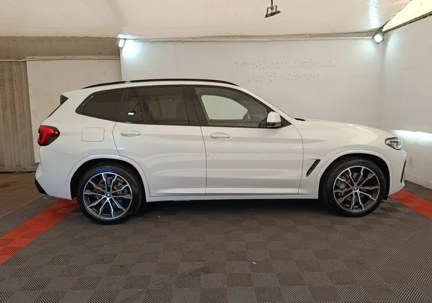 BMW X3 xDrive30e blanc vue de profil côté gauche dans un garage avec jantes alliage et toit noir.