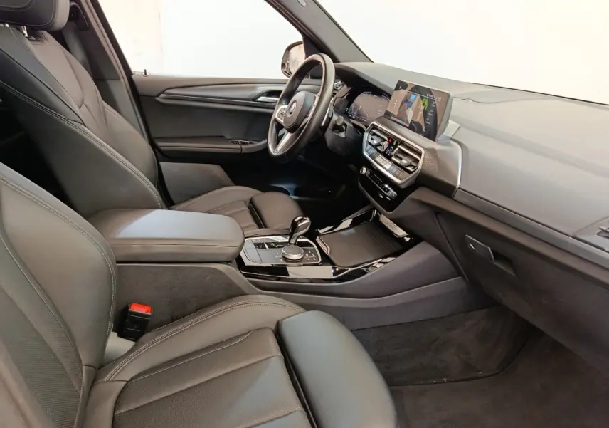 Intérieur BMW X3 xDrive30e 2023 vu côté passager, sièges cuir noirs et tableau de bord avec écran tactile.