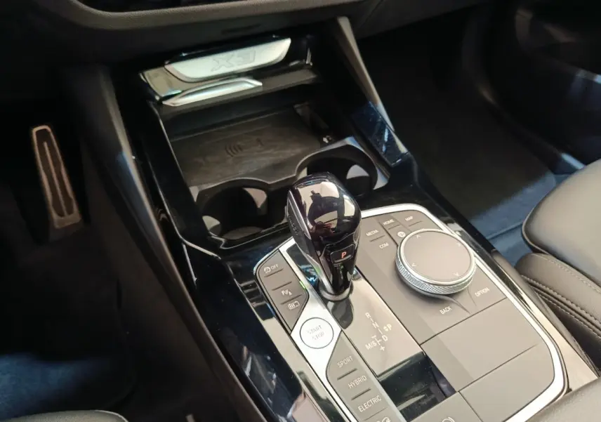 Gros plan sur la console centrale noire du BMW X3 blanc, avec levier de vitesses et molette de contrôle visibles.