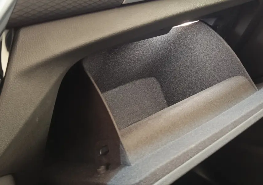 Gros plan sur la boîte à gants ouverte du BMW X3 xDrive30e blanc, montrant l'intérieur texturé noir.