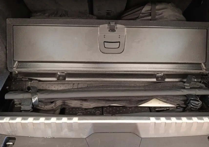 Coffre ouvert d’un BMW X3 blanc, montrant un compartiment de rangement sous plancher avec filet de sécurité noir.