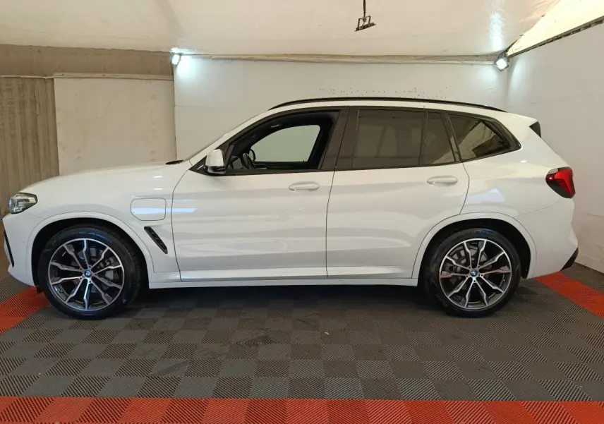 BMW X3 xDrive30e blanc en vue profil côté gauche, avec jantes alliage et prise de recharge visible.