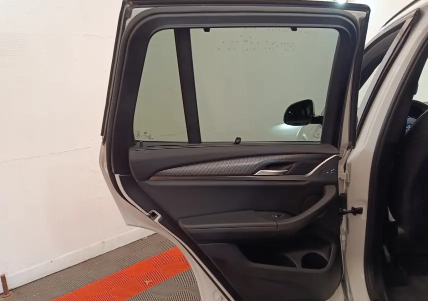 Vue intérieure de la porte arrière droite ouverte d'un BMW X3 blanc, avec garniture noire et détails argentés.