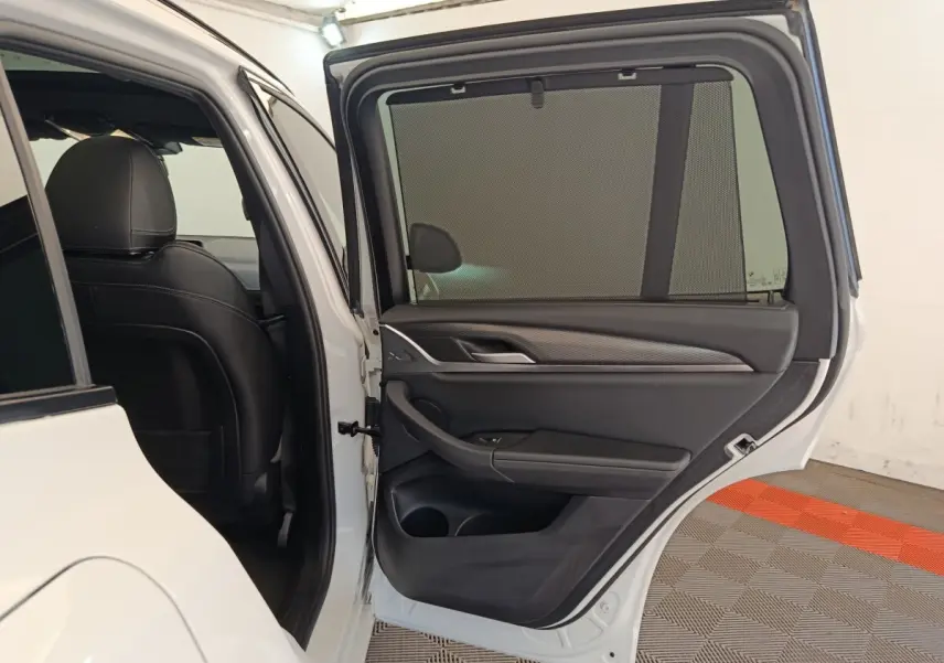 Porte arrière droite ouverte d’un BMW X3 blanc 2023, montrant l’habillage intérieur noir avec pare-soleil intégré.