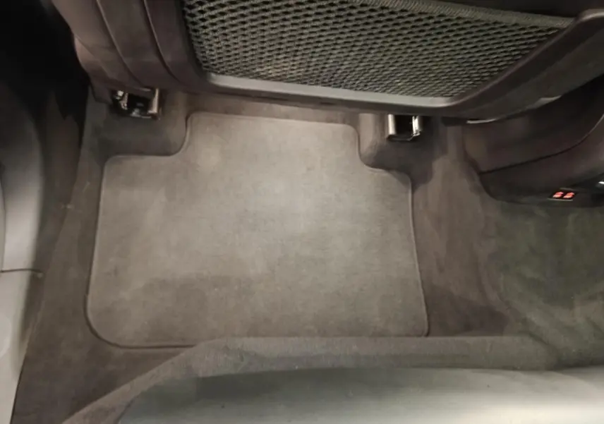 Vue plongeante sur le tapis de sol arrière gris foncé du BMW X3 xDrive30e blanc, avec filet de rangement sous le siège avant.