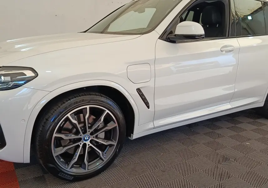 Vue latérale gauche rapprochée du BMW X3 blanc xDrive30e 2023 avec jante alliage et prise de recharge visible.