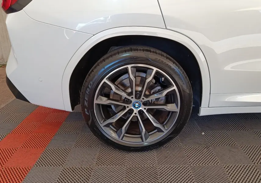 Gros plan sur la roue arrière droite d’un BMW X3 blanc, mettant en valeur la jante alliage M Sport et le pneu Pirelli P Zero.
