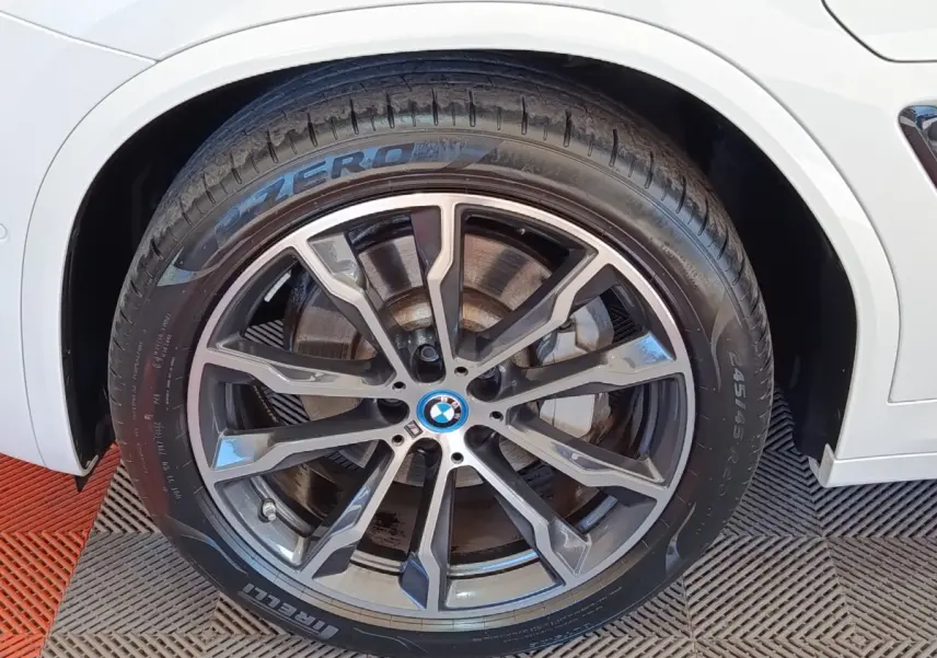 Gros plan sur la roue avant droite du BMW X3 blanc, jante alliage sombre à design sportif et pneu Pirelli P Zero.