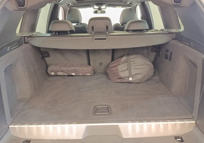 Vue arrière du coffre spacieux d’un BMW X3 blanc 2023 avec cache-bagages et objets rangés.