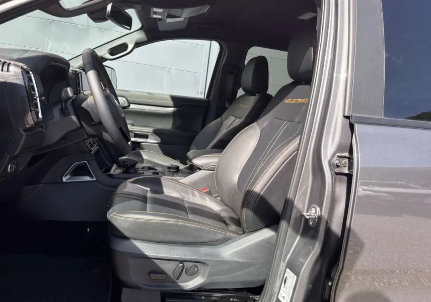 Vue intérieure côté conducteur du Ford Ranger gris carbone 2026, sièges cuir Wildtrak avec surpiqûres orange.