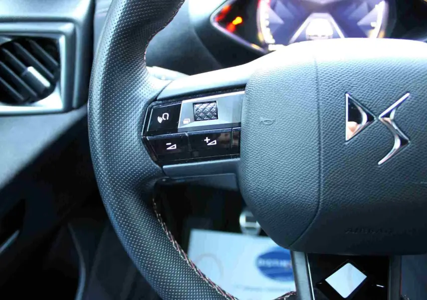 Gros plan sur le volant noir texturé du DS3 Crossback gris platinium, avec commandes intégrées et logo DS visible.