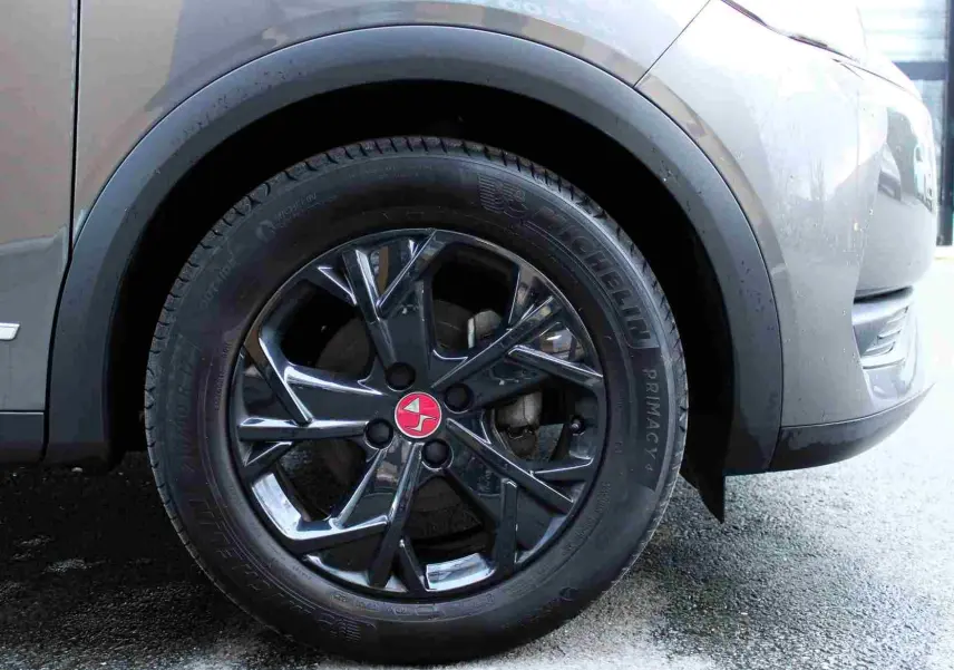 Gros plan sur la roue avant droite d’un DS3 Crossback gris platinium métal avec jante noire brillante et logo rouge central.
