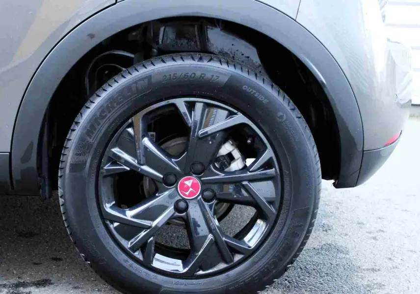 Gros plan sur la roue arrière droite du DS3 Crossback gris platinium avec jante noire brillante et logo rouge au centre.